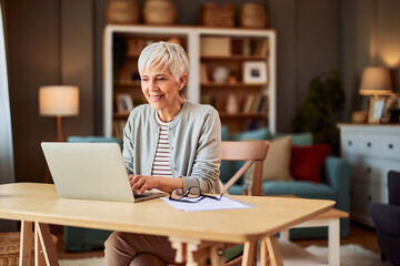 A smiling senior woman with short hair working from home while using a laptop