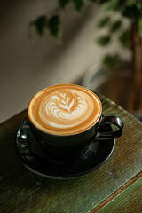 Cup of Cappuccino with beautiful cream latte art on a wooden coffee shop table. Dark green Background. Selective focus.