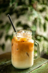 Iced coffee on the wooden table in a coffee shop. Cold summer drink. Green plant background.