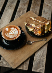 Cup of Cappuccino with beautiful cream latte art with a piece of cake, on coffee shop table. Wooden background.