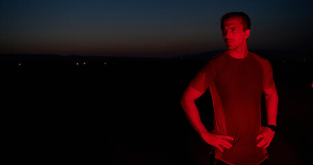 Athlete Strikes a Pose Under Red Nighttime Glow After Intense Daylong Marathon. - obrazy, fototapety, plakaty