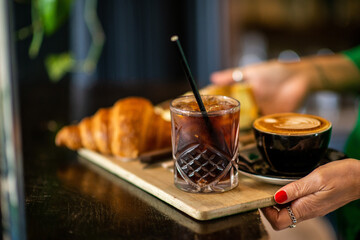 Woman holds a tray with cups of coffee and pastries, in a coffee shop. Cold drink. Selective focus.