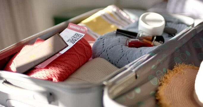 A suitcase lies open, revealing neatly packed clothes, a boarding pass, and travel essentials