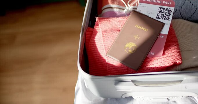 A passport and boarding pass rest atop clothes in an open suitcase