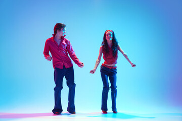 Stylish handsome young man and beautiful woman dancing rock and roll retro dance against blue background in neon light. Concept of hobby, dance class, party, 50s, 60s culture, youth