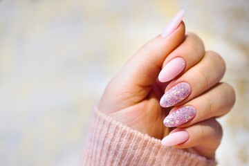 A woman's hand with beautiful pink gel nails. Well-groomed and perfectly painted nails, two adorned with stylish, multicolored glitter.
