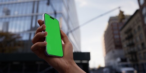 Hand showcasing a smartphone with a green screen, urban city street background - 757142154