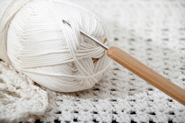 A skein of white thread and a crochet hook with a wooden handle