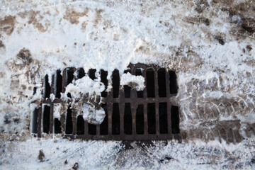 Drain grate on the road covered with snow.
