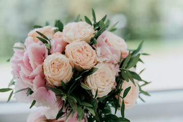wedding bouquet of peach and pink roses with green leaves near the window close-up