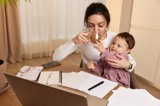 beautiful businesswoman working at home with her little child girl and drinking coffee