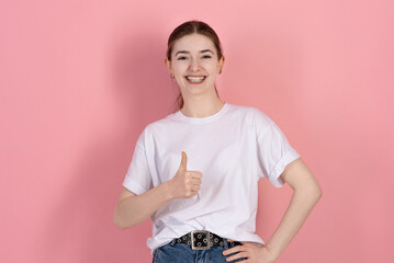 Attractive Caucasian young brunette woman in casual white t-shirt looks at the camera, smiles and...