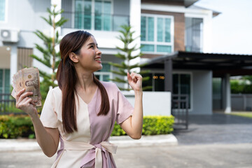 Portrait of happy attractive Asian women holding a lot of banknotes in front of home to celebrate and Pay the final installment of the house, Loans for real estate concept, Smiling young successful