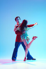 Artistic, talented, positive young man and woman, stylish couple dancing retro dance against blue background in neon light. Concept of hobby, dance class, party, 50s, 60s culture, youth