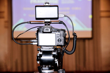 Camera with blank screen on a tripod in a conference room. Selective focus.