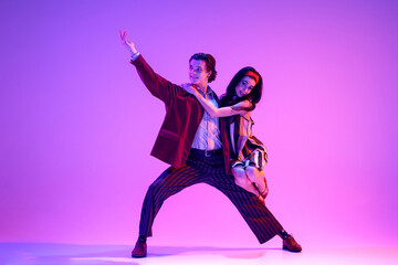 Artistic young man and woman in retro style clothes dancing boogie woogie against purple background...