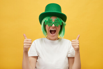 Overjoyed excited woman with green hair wearing leprechaun hat and shamrock glasses posing isolated...