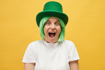 Overjoyed excited amazed beautiful woman with green hair wearing leprechaun hat standing isolated...