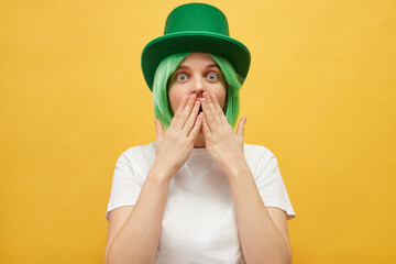 Shocked frighten woman with green hair wearing leprechaun hat posing isolated over yellow...