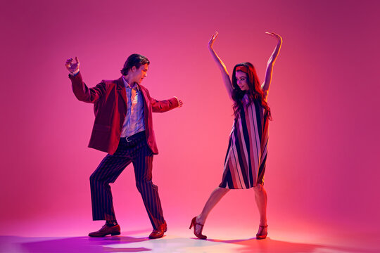 Young man and woman in stylish clothes dancing retro dance, boogie woogie against pink background in neon light. Concept of hobby, dance class, party, 50s, 60s culture, youth