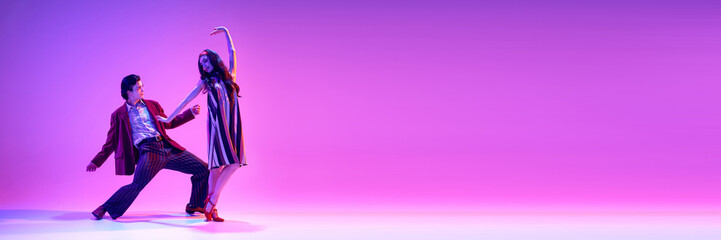 Retro dance aesthetics. Elegant young man and woman dancing against purple background in neon. Concept of hobby, dance class, party, 50s, 60s culture, youth. Banner. Empty space to insert text ad