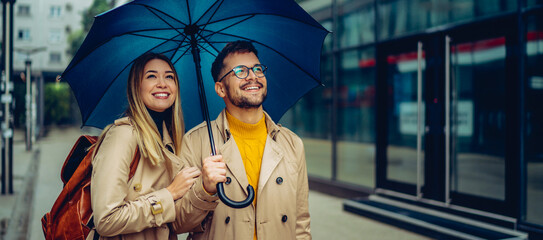 Happy young couple standing under an umbrella and looking around the city. © kerkezz