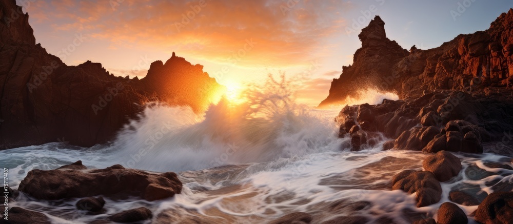 Sticker At dusk, a picturesque sunset illuminates the sky with hues of orange and pink over a rocky beach. Waves crash against the rocks, creating a mesmerizing atmosphere