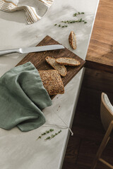 Fototapeta na wymiar Sliced bread on wooden board in linen bag, fresh herbs and stainless still kitchen knife. Kitchen aesthetic concept