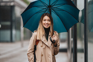 Portrait of beautiful young girl walking with umbrella under rain