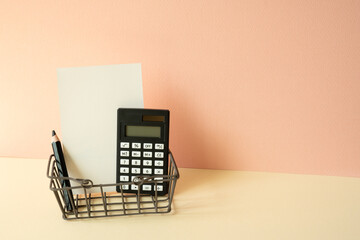 Consumer shopping basket with calculator, pencil, memo pad on ivory and pink background. Economic...