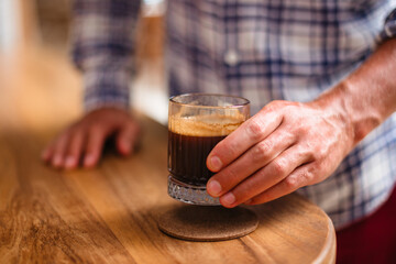 Male hand holding hot glass with black coffee. Delicious strong coffee made from high-quality beans - obrazy, fototapety, plakaty