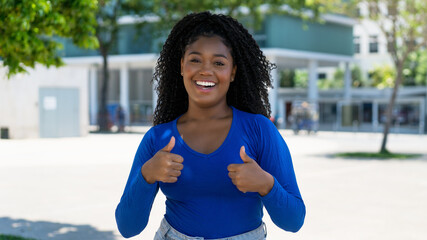 Laughing african american young adult woman showing thumbs up in the city