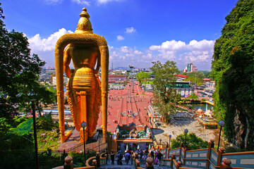 Rear view of the large golden statue of Murugan and people on the stairs going up to the Batu...