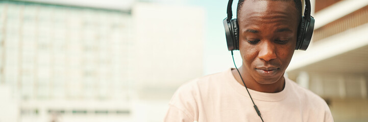 Portrait of young african student sitting outside of university and taking notes while study online with headphones, Panorama