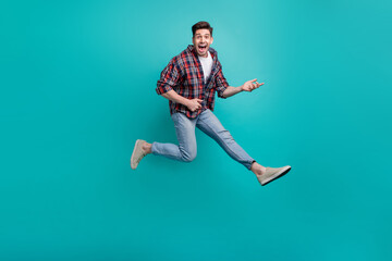 Full length photo of funky good mood guy wear checkered shirt jumping high playing guitar isolated teal color background