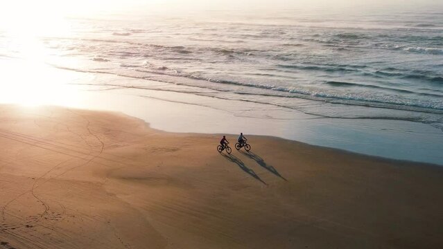 Couple cycles on the beach at sunrise