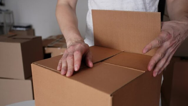 Close-up hands of unrecognizable man assembling little cardboard box for personal stuff storing at relocation day, leaves to new own or rented house, prepare dwelling for remodeling or removal work.