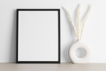Black frame mockup with a pampas decoration on the beige table.