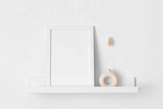 White frame mockup with a lagurus decoration on the wall shelf.
