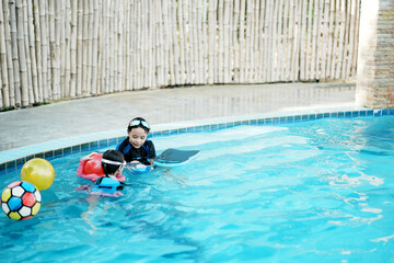 A little asian boy and girl in swimming in the pool. Cute girl playing in outdoor swimming pool on a hot summer day. Kids learn to swim.