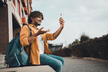 Photo of funny cheerful indian man international exchange student speaking video call outdoors...