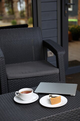 breakfast on the terrace, black tea, and cheesecake and a laptop. aesthetic breakfast on the street. white cup with tea. country recreation. rest and relaxation. working on a laptop and drinking tea.