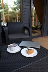 breakfast on the terrace, black tea, and cheesecake and a laptop. aesthetic breakfast on the street. white cup with tea. country recreation. rest and relaxation. working on a laptop and drinking tea.