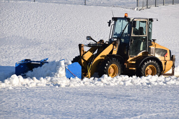Blue wheel loader snow pusher pushing heavy snow in a parking lot. - obrazy, fototapety, plakaty