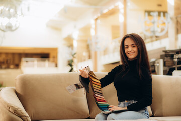 Obraz premium The woman chooses the fabric on the sofa. A young women looks at tissue samples. Selects the color of the sofa. Textile industry background. Tissue catalog