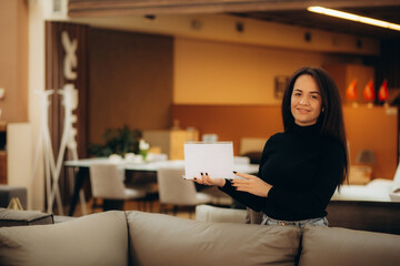 A woman seller of sofas with a white sign in her hands in a furniture store