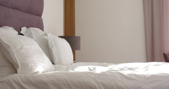 A neatly made bed with white linens is in focus, with a purple headboard, with copy space