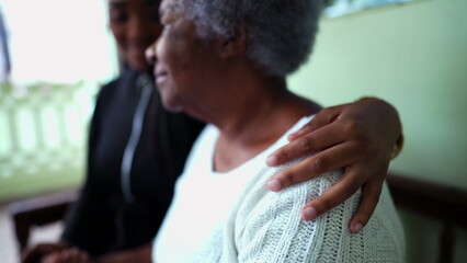 African American granddaughter caring for elderly grandmother in old age with arm around shoulder showing help and support for senior woman in 80s, inter-generational family care