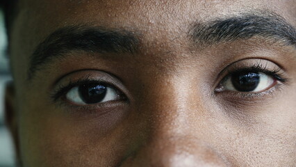 Macro closeup of a young black man eyes staring at camera with intense gaze in solemn serious expression, eye to eye - facial features