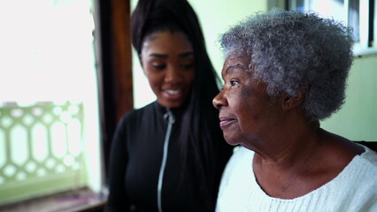 African American granddaughter caring for elderly grandmother in old age with arm around shoulder...